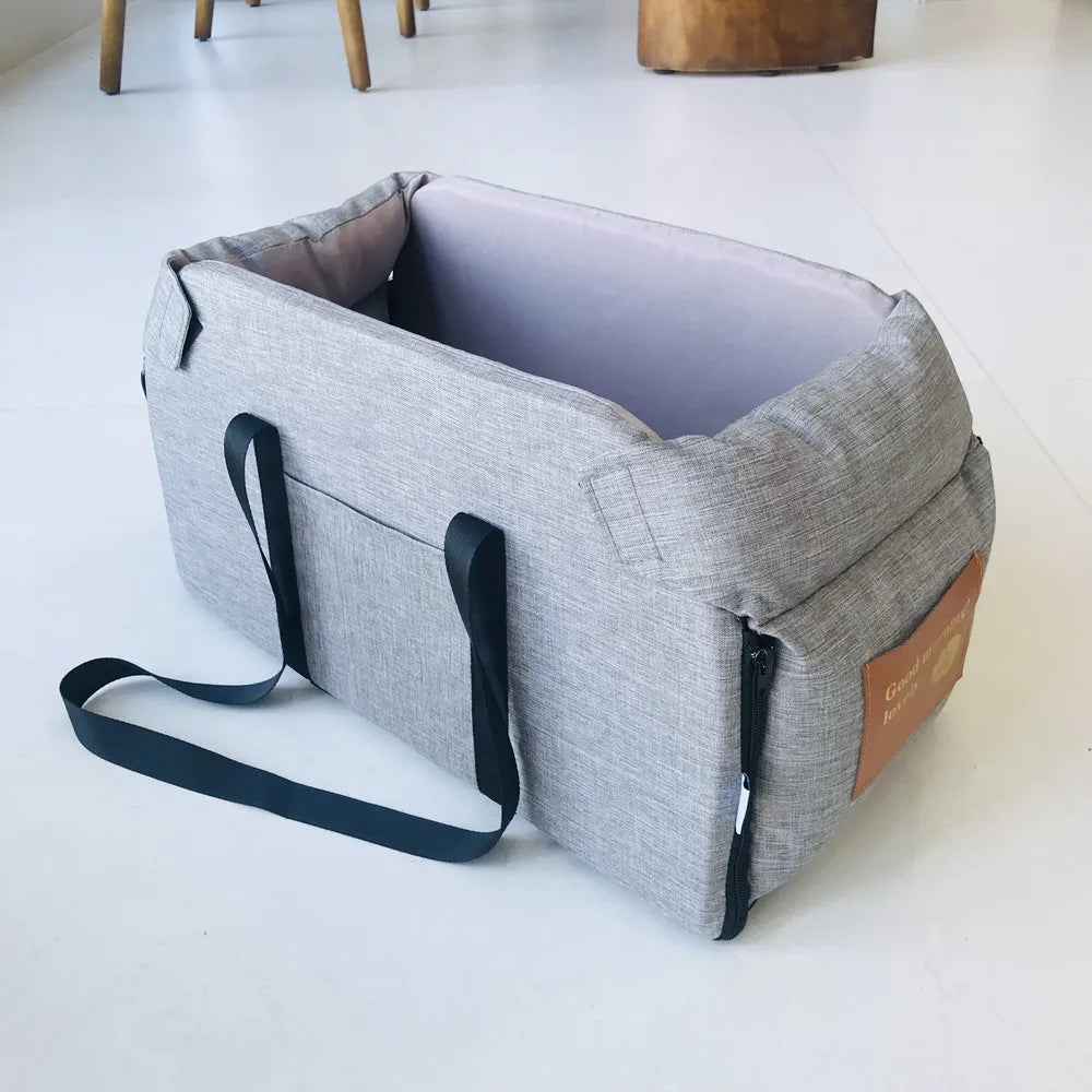 Gray portable pet carrier with black straps on a white floor, Carcader product