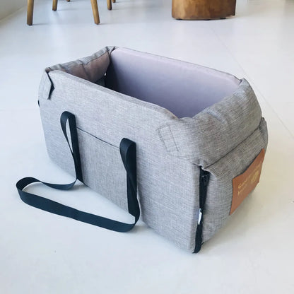 Gray portable pet carrier with black straps on a white floor, Carcader product